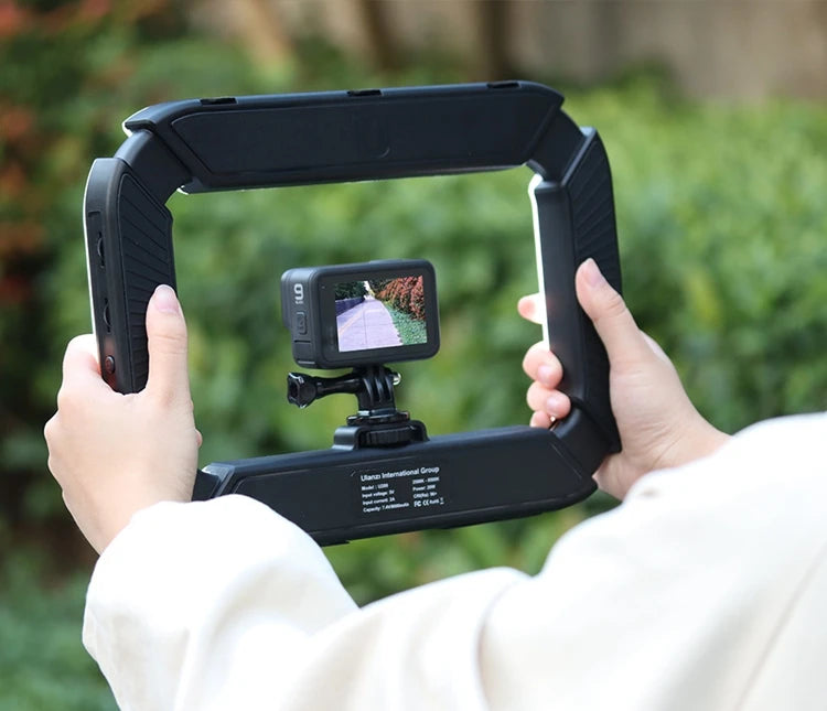 Hands holding a black stabilizing rig with a GoPro camera attached, displaying a butterfly on screen, outdoors.