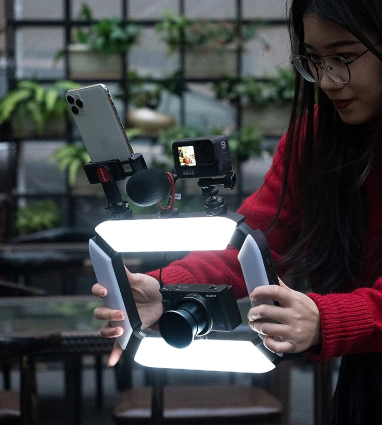 A woman using a camera rig with a smartphone, microphone, action camera, and digital camera, equipped with LED lights, to capture photos indoors.