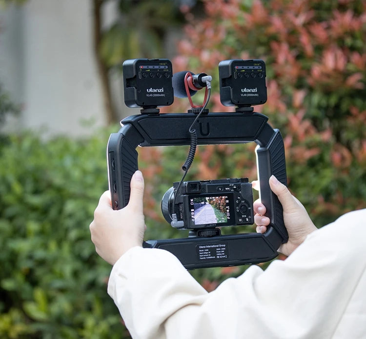 Hands holding a black stabilizing rig with a GoPro camera attached, displaying a butterfly on screen, outdoors